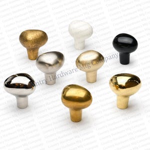 May include: Assortment of eight cabinet knobs in various metallic finishes, including gold, silver, and black. The knobs have a mushroom-shaped design and are arranged on a white background.