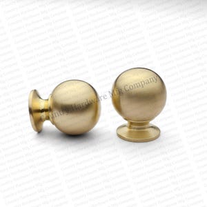 May include: Two gold-colored cabinet knobs with a spherical design. The knobs have a round base and a smooth, polished finish. They are suitable for furniture or cabinet hardware.