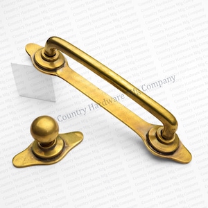 May include: A set of antique brass hardware, including a pull handle and a knob. The pull handle is a curved bar with decorative mounts, and the knob has a rounded top and a decorative base. The hardware is likely for a cabinet or drawer.