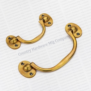 May include: Two antique brass cabinet handles with a curved design. The handles have a rounded oval shape at the top and bottom.