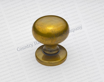 May include: A round cabinet knob with a smooth, polished brass finish. The hardware features a spherical head attached to a circular base plate, showcasing a warm, metallic gold tone with subtle darkened patina accents around the neck and base.