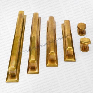 May include: Four brass door pulls with a geometric design and two brass knobs. The pulls are rectangular with a beveled edge and the knobs are round and hexagonal. The hardware is made by Country Hardware Mfg Company.