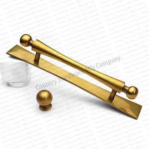May include: A set of brass-toned door hardware, including a long pull handle, a knob, and a rectangular backplate. The handle has a cylindrical center and ball-shaped ends. The knob is spherical.