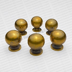 May include: Five antique gold-toned cabinet knobs with a round ball shape and a small base. The knobs are arranged in a circle on a white background.