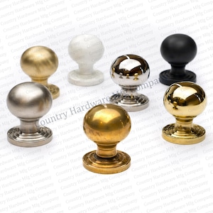May include: A collection of seven cabinet knobs in various metallic finishes, including gold, silver, and black. Each knob has a round ball shape and a decorative base. The knobs are displayed against a white background.