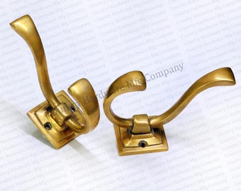 May include: Two brass coat hooks with a curved design. The hooks are mounted on square bases.