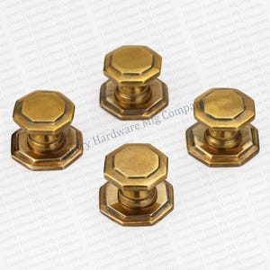 May include: Four brass door knobs with an octagonal shape and a raised edge. The knobs have a polished finish and are designed for use on doors.