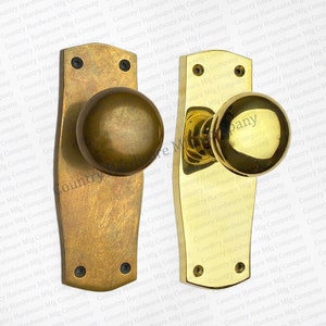 May include: Two antique brass door knobs with matching backplates. One knob has a darker, aged finish, while the other is polished to a bright gold. The backplates are rectangular with rounded edges and screw holes. The image shows the "Country Hardware Mfg Company" logo.