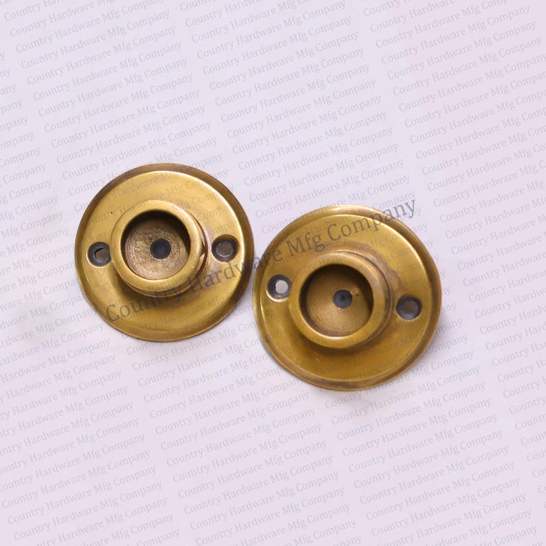 May include: Two brass curtain rod finials with a round, flat base and a center hole. The finials have a smooth, polished finish.