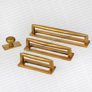 May include: Four gold-toned cabinet pulls with a rectangular shape and a raised bar handle. The pulls are arranged in a descending size order, with the largest pull at the top and the smallest pull at the bottom. The pulls are all made of the same metal and have a polished finish.