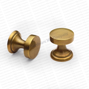 May include: Two antique brass cabinet knobs. Each knob has a cylindrical base and a rounded top. The knobs are made of brass and have a warm, aged finish. These knobs are suitable for furniture restoration or adding a vintage touch.