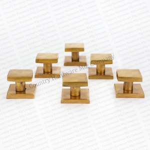 May include: Six brass cabinet knobs with a square base and a round knob. The knobs are a brushed gold color.