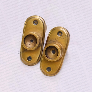 May include: Two oval-shaped brass curtain rod holders with a decorative edge. Each holder has a round opening in the center.