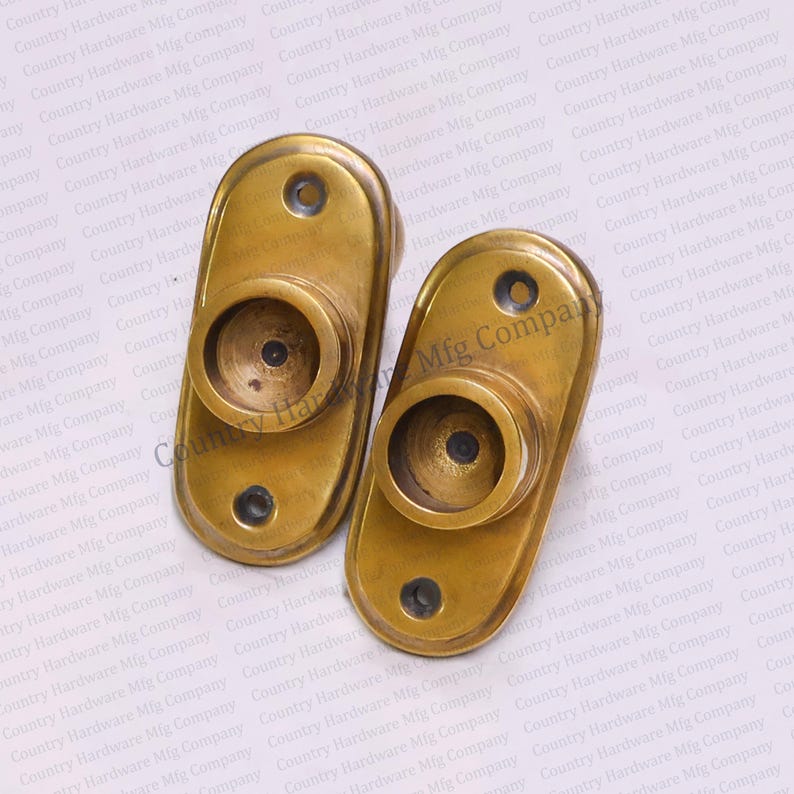 May include: Two oval-shaped brass curtain rod holders with a decorative edge. Each holder has a round opening in the center.
