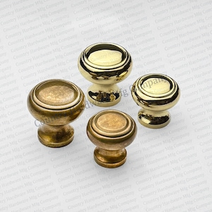 May include: Four brass cabinet knobs in varying sizes. The knobs have a rounded top with a circular design and a short, decorative base. The knobs have a shiny, metallic finish, and the text "Country Hardware Mfg Company" is visible on the top of some knobs.