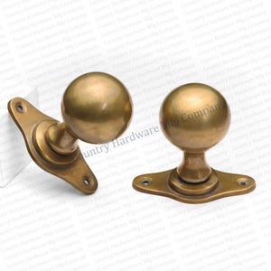 May include: Two antique brass door knobs with a spherical design. Each knob has a round handle and a rectangular base with screw holes. The hardware has a vintage aesthetic, suitable for home renovation projects.
