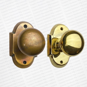 May include: Two antique brass door knobs with a round shape and a decorative design. The knobs are mounted on a rectangular plate with a rounded edge.