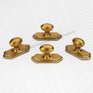 May include: Three gold-toned cabinet knobs with a rectangular base and an oval-shaped handle. The knobs have a slightly textured finish.