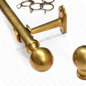 May include: A set of brass-colored curtain rods, brackets, and finials. The rods are cylindrical, and the finials are spherical. The brackets are designed to mount the rods to a wall. The hardware is made of metal.