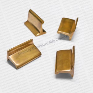 May include: Four brass cabinet door pulls with a rectangular shape and a raised edge. The pulls have a brushed finish.