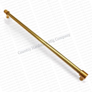 May include: A gold-colored cabinet pull with a cylindrical bar and rounded end pieces. The hardware is designed for installation on a cabinet or drawer. The pull is made of metal and has a smooth finish.