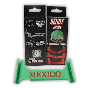 May include: A green plastic tool with the word "MÉXICO" printed in red. The tool is used to bend the brim of a baseball cap. Two boxes are shown in the background. One box is black with white text and a QR code. The other box is black with red text and shows a green baseball cap with a red brim.