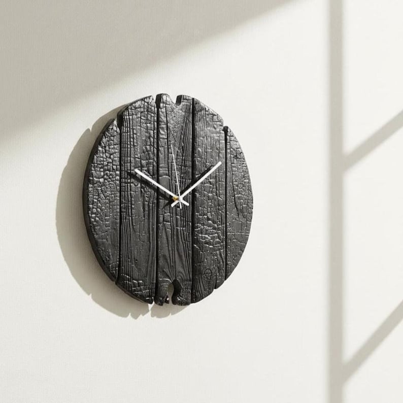 May include: A round, black wooden wall clock with white hands. The clock face is made of vertical wooden planks, giving it a rustic appearance. The clock is mounted on a white wall.