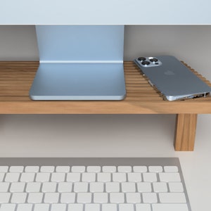 May include: A wooden monitor stand with a silver computer monitor and a silver smartphone on top. A white keyboard and a white mouse are on the desk below the stand.