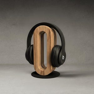 May include: A wooden headphone stand with a black base and a natural wood finish. Black headphones with the Beats logo are displayed on the stand. The stand has a unique, modern design.