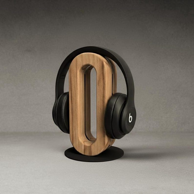 May include: A wooden headphone stand with a black base and a natural wood finish. Black headphones with the Beats logo are displayed on the stand. The stand has a unique, modern design.