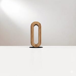 May include: A wooden letter O, standing upright on a white surface. The letter has a light brown color with visible wood grain. The background is a neutral off-white, with a shadow cast by the letter.