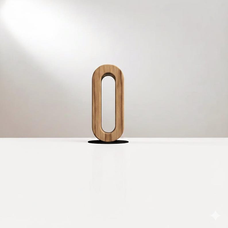 May include: A wooden letter O, standing upright on a white surface. The letter has a light brown color with visible wood grain. The background is a neutral off-white, with a shadow cast by the letter.