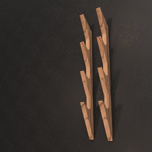 May include: Two wooden wall hooks with a branch-like design. Each hook has five curved branches that extend out from the main stem. The hooks are a light brown color and are mounted on a dark gray wall.