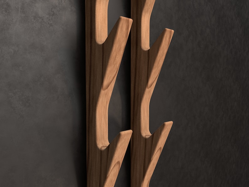 May include: Two wooden wall hooks shaped like branches with multiple hooks. The hooks are a light brown color and are mounted on a dark gray wall.