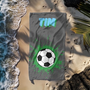 Könnte beinhalten: Graues Strandtuch mit einem grünen und weißen Fußball-Motiv und dem Namen "TIM" in blauen Buchstaben.