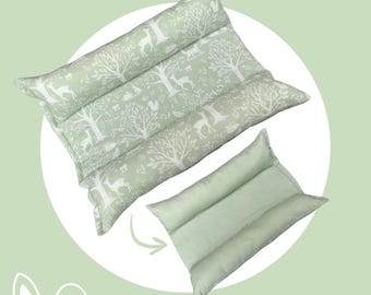 May include: A rectangular sage green pillow featuring a white woodland print of deer, trees, and small animals, shown alongside a smaller, solid sage green rectangular pillow with a three-section stitched design and a curved arrow graphic.