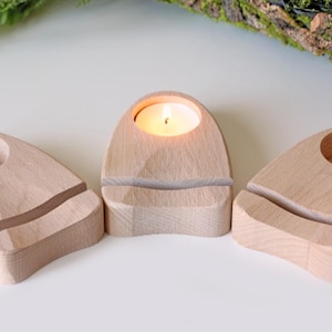 Könnte beinhalten: Drei Holz-Kerzenhalter in Raketenform, wobei ein Halter mit einer kleinen weißen Kerze angezündet ist.