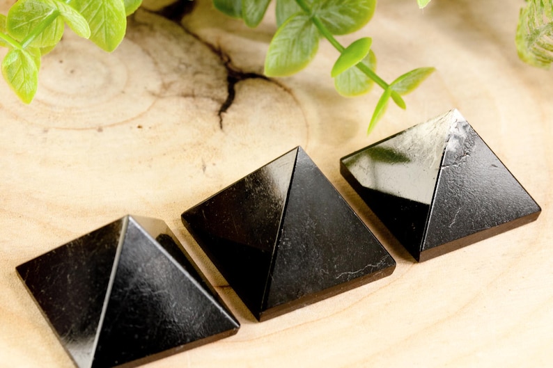 May include: Three black obsidian pyramids of varying sizes on a light wood surface.