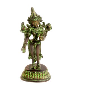 Pode incluir: Estátua de bronze de uma divindade com detalhes verdes. A figura é adornada com joias detalhadas e um cocar, em pé sobre uma base decorativa. A estátua tem aproximadamente 15 cm de altura.