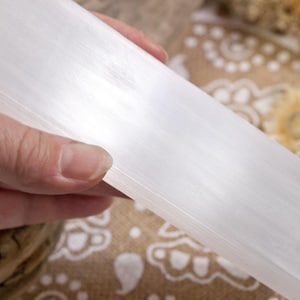 Op de afbeelding: Een witte seleniet-laadplaat, een glad, rechthoekig stuk kristal, vastgehouden in een hand.