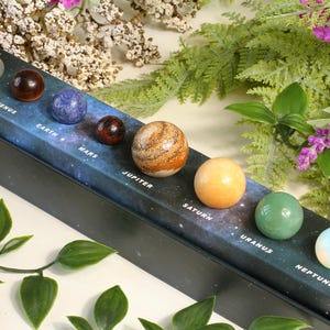 May include: A decorative box featuring a miniature solar system with gemstone planets. The planets are arranged in order, with labels like "Mercury" and "Venus" on a starry background. The planets are various colors and textures.
