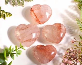 May include: Four polished heart-shaped stones with a translucent pale pink base and deep reddish-brown mineral inclusions. The stones are arranged in a cluster, showcasing smooth, rounded surfaces and natural internal veining patterns.