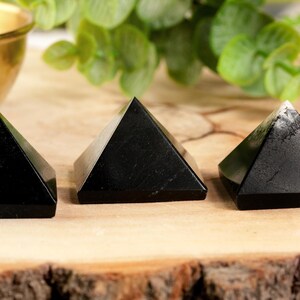 May include: Three black obsidian pyramids on a wooden surface. The pyramids are smooth and polished.