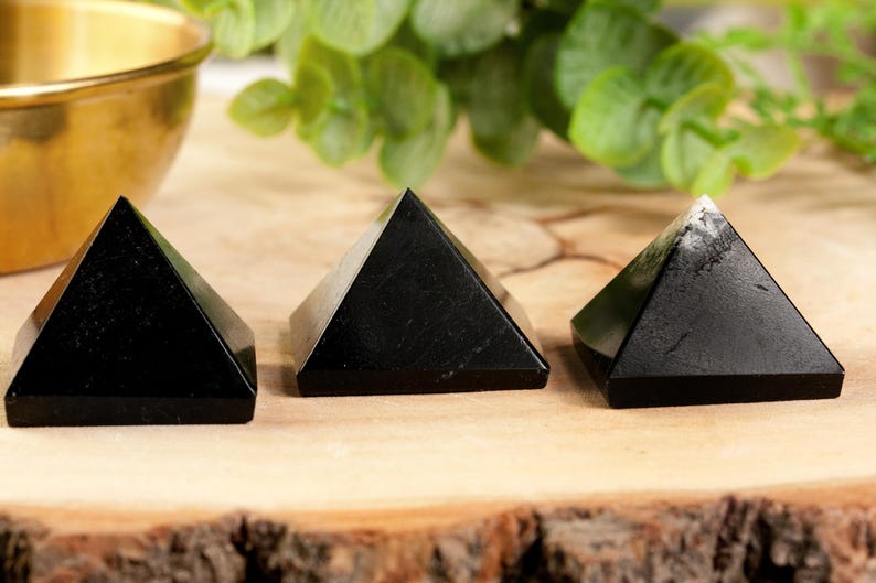 May include: Three black obsidian pyramids on a wooden surface. The pyramids are smooth and polished.