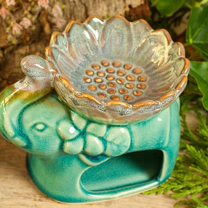 Op de afbeelding: Turquoise keramische oliefilter in de vorm van een olifant met een zonnebloemvormige bovenkant. De bovenkant heeft een klein putje voor wax melts en een decoratief ontwerp van kleine bruine stippen.