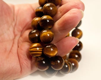 May include: A bracelet composed of polished, spherical tiger's eye beads. The beads exhibit a characteristic chatoyant lustre with alternating bands of golden-brown and dark brown colours, strung together in a continuous circular loop.