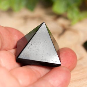 May include: Two black obsidian pyramids, one held in a hand, the other on a wooden surface.