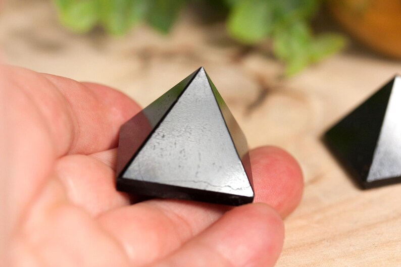 May include: Two black obsidian pyramids, one held in a hand, the other on a wooden surface.