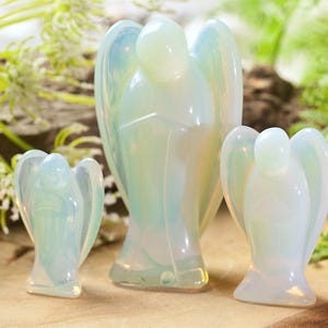 Pode incluir: Três figuras de anjos de opala branca de tamanhos diferentes. O anjo maior está no centro, com um anjo menor de cada lado.