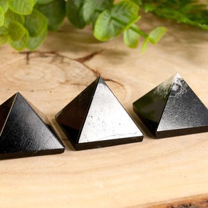 May include: Three black obsidian pyramids of varying sizes on a wooden surface. The pyramids are smooth and polished.